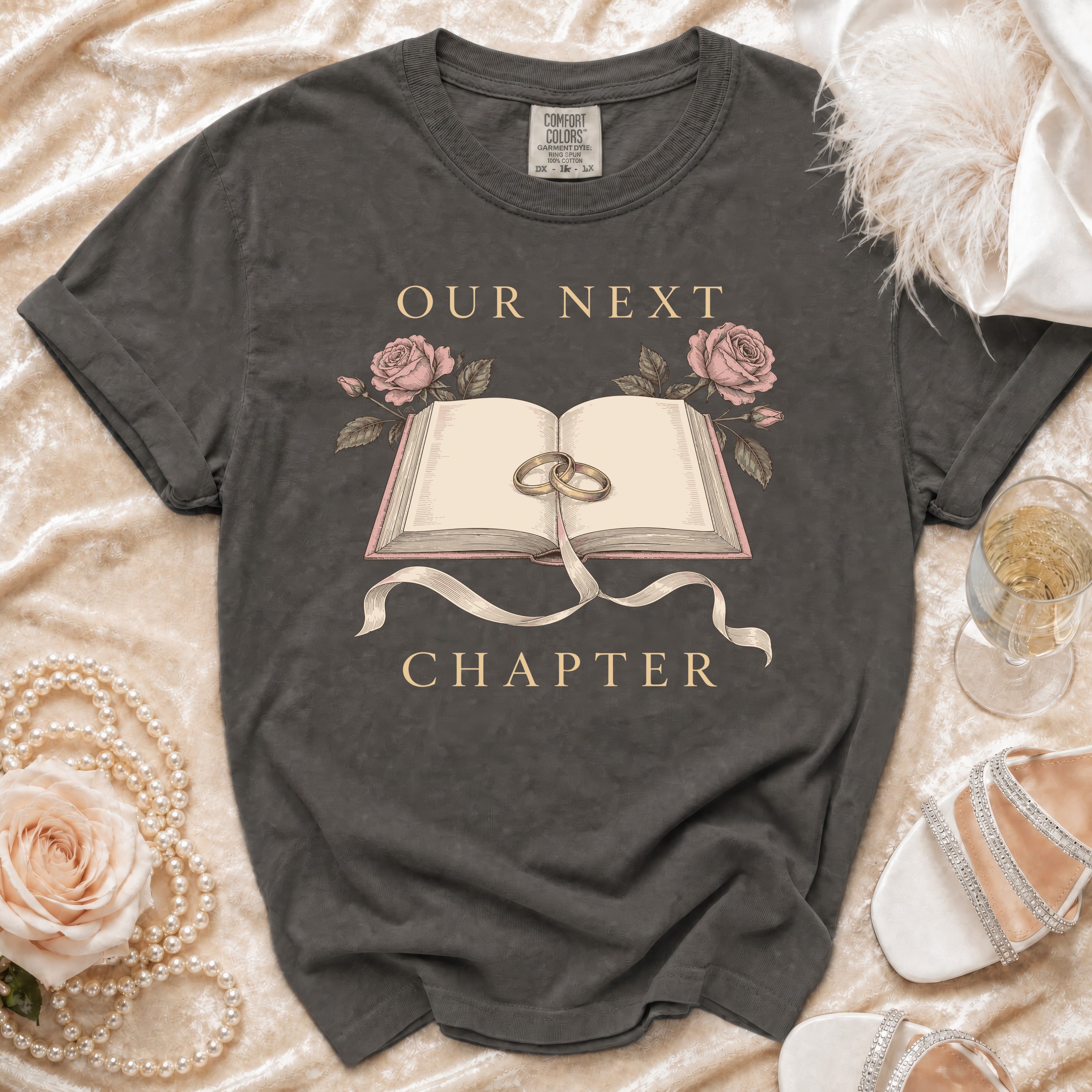 Dark grey t-shirt with "Our Next Chapter" text and wedding rings on an open book.