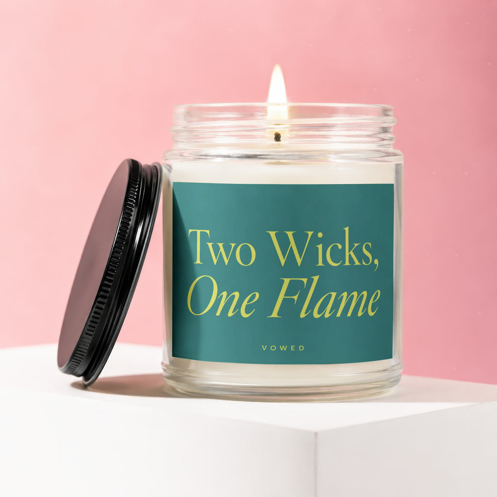 Burning two-wick candle in glass jar with teal label reading "Two Wicks, One Flame".