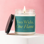 Burning two-wick candle in glass jar with teal label reading "Two Wicks, One Flame".