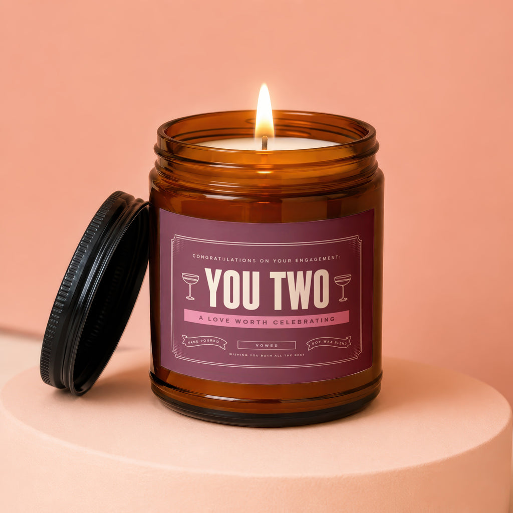 Amber jar candle with "You Two" label and lit flame.