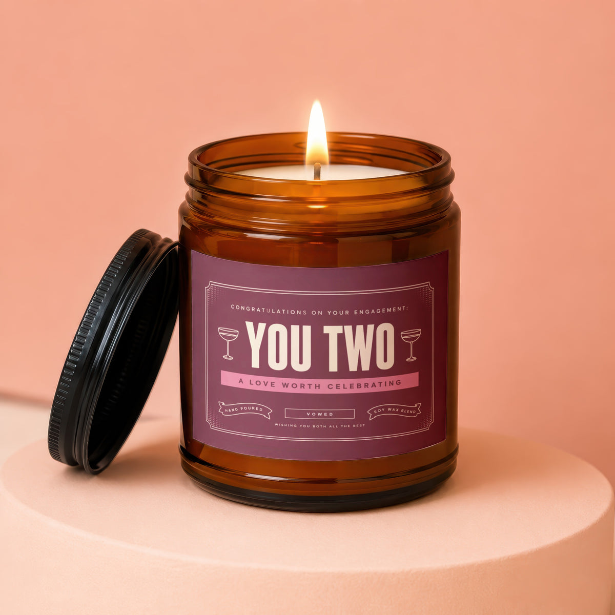 Amber jar candle with "You Two" label and lit flame.