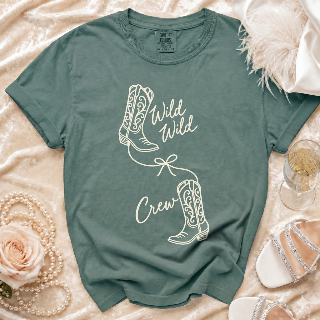 A sage green t-shirt features white graphics of two cowboy boots and the text Wild Wild Crew.