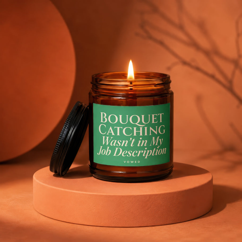 Amber jar candle with lit flame and green label reading "BOUQUET CATCHING Wasn't in My Job Description".