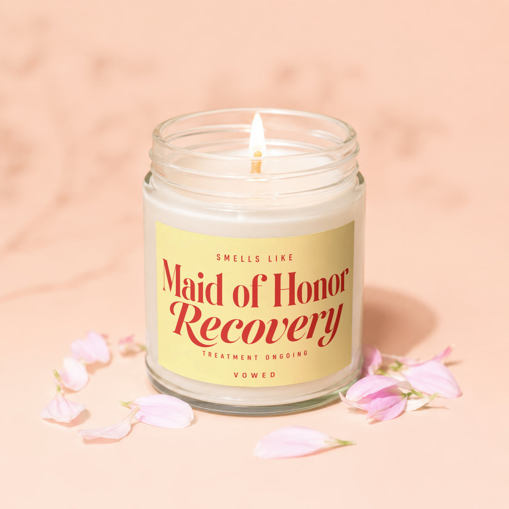 Candle with yellow label that reads "SMELLS LIKE Maid of Honor Recovery TREATMENT ONGOING VOWED".