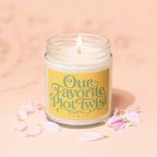 Jar candle with lit wick, yellow label reading "Our Favorite Plot Twist"