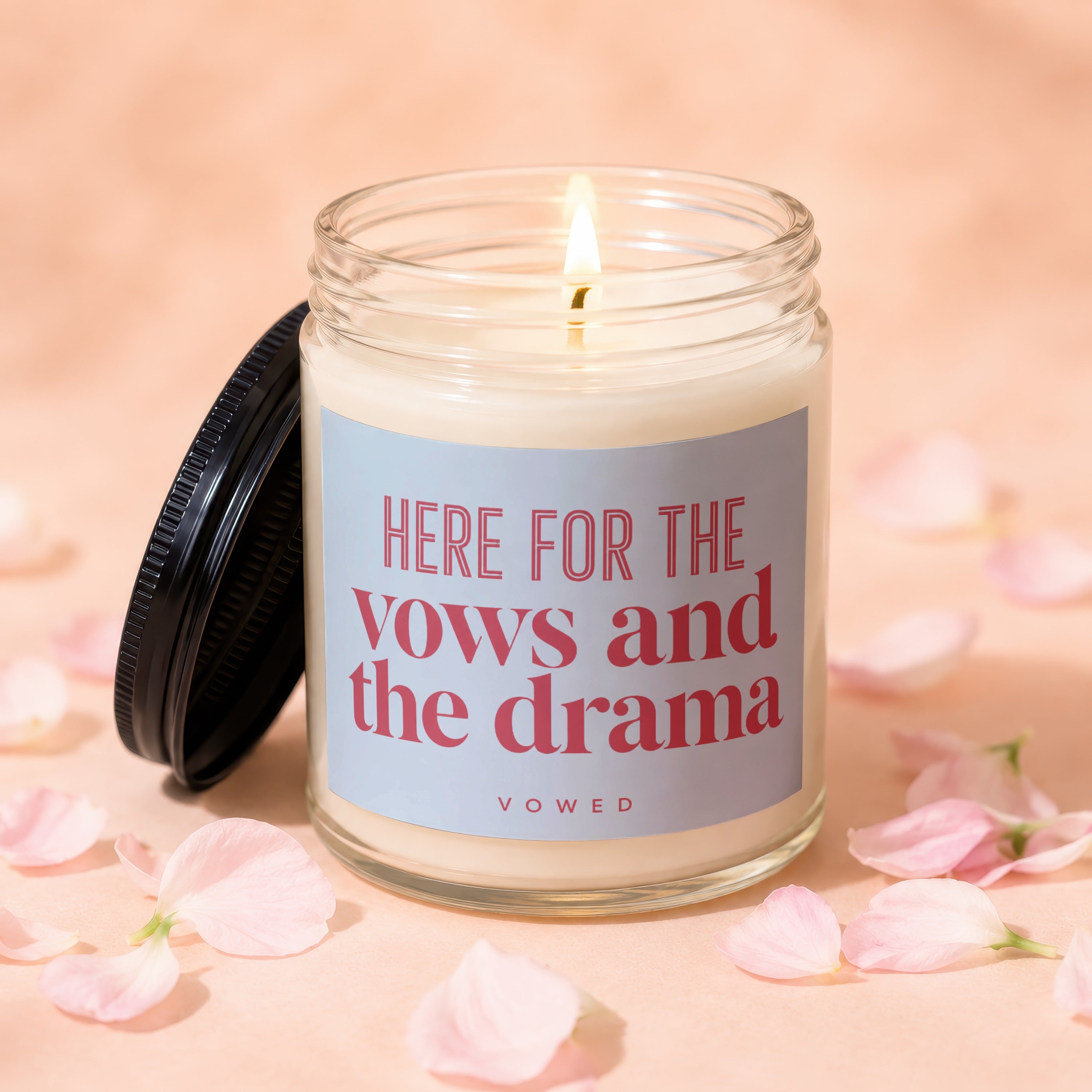 Lit candle in glass jar with black lid, reading "HERE FOR THE vows and the drama VOWED".
