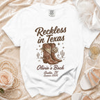 White t-shirt with "Reckless in Texas" and "Olivia's Bach Austin, TX Summer 2026".