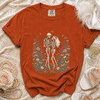 Orange t-shirt with skeleton couple wedding graphic surrounded by flowers.