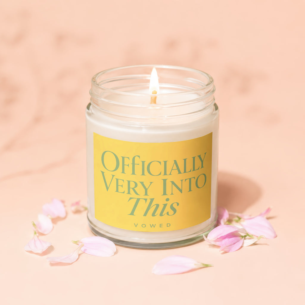 Glass jar candle with burning wick and label stating "Officially Very Into This Vowed".