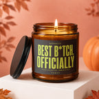 Amber glass candle with "Best B*tch, Officially" text and lit wick.