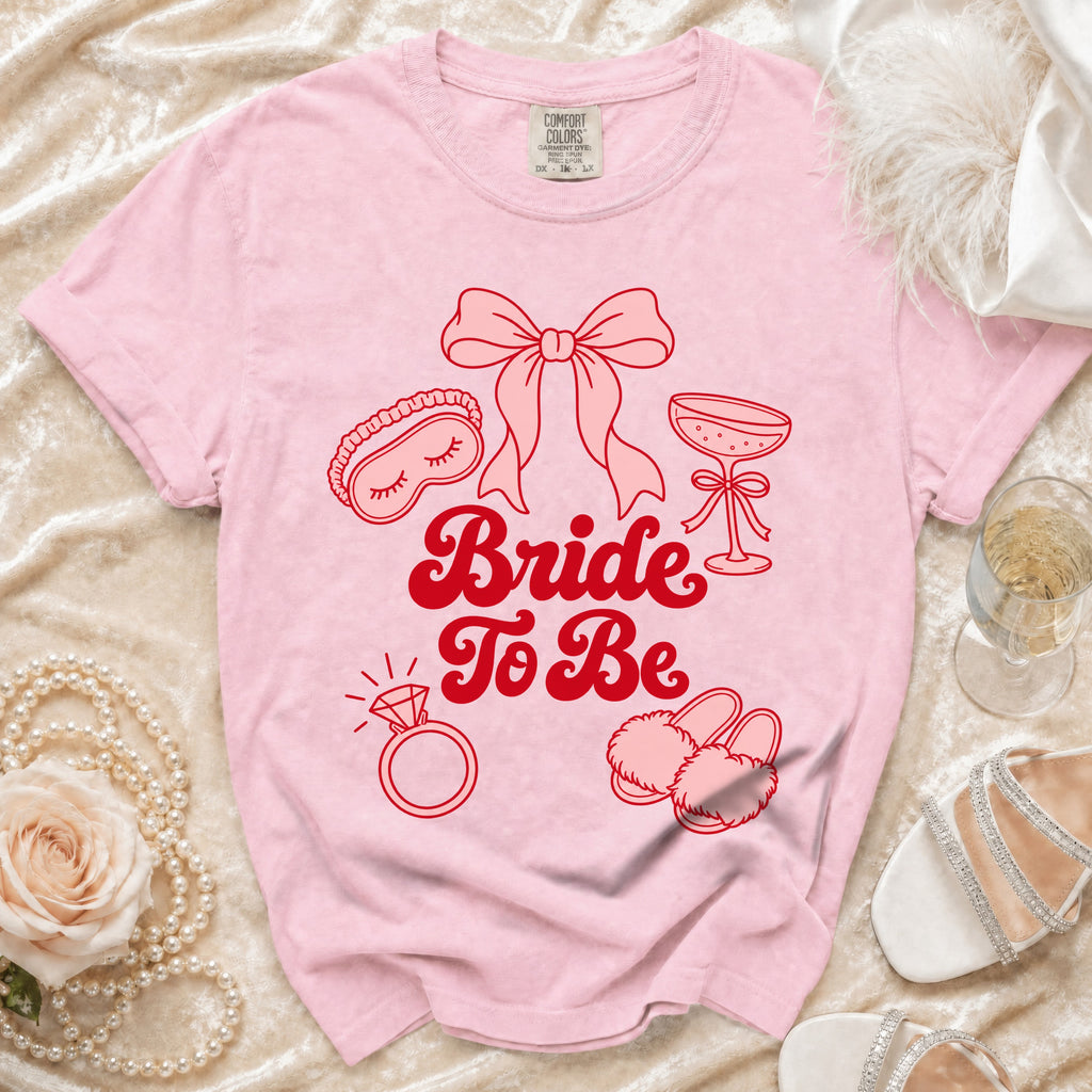 Pink t-shirt with "Bride To Be" text and icons of wedding items.