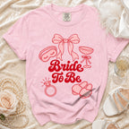 Pink t-shirt with "Bride To Be" text and icons of wedding items.