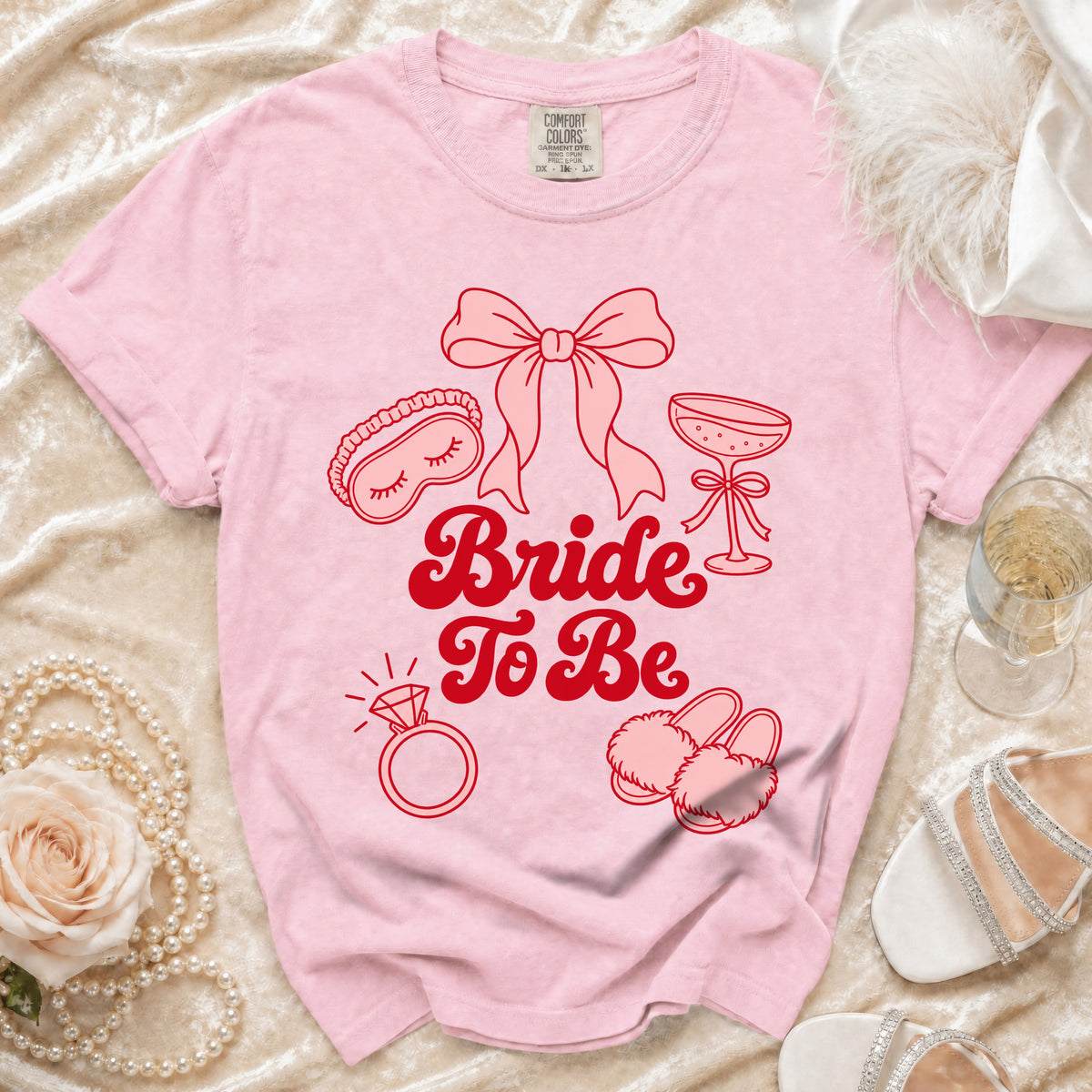 Pink t-shirt with "Bride To Be" text and icons of wedding items.