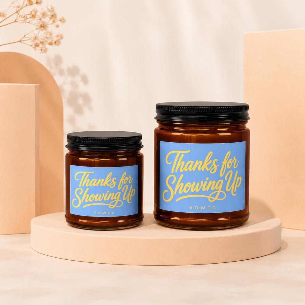 Two amber glass candles with black lids and blue labels reading "Thanks for Showing Up."