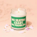 Candle with lit wick and green label reading "NO SEATING CHART. NO PROBLEM."