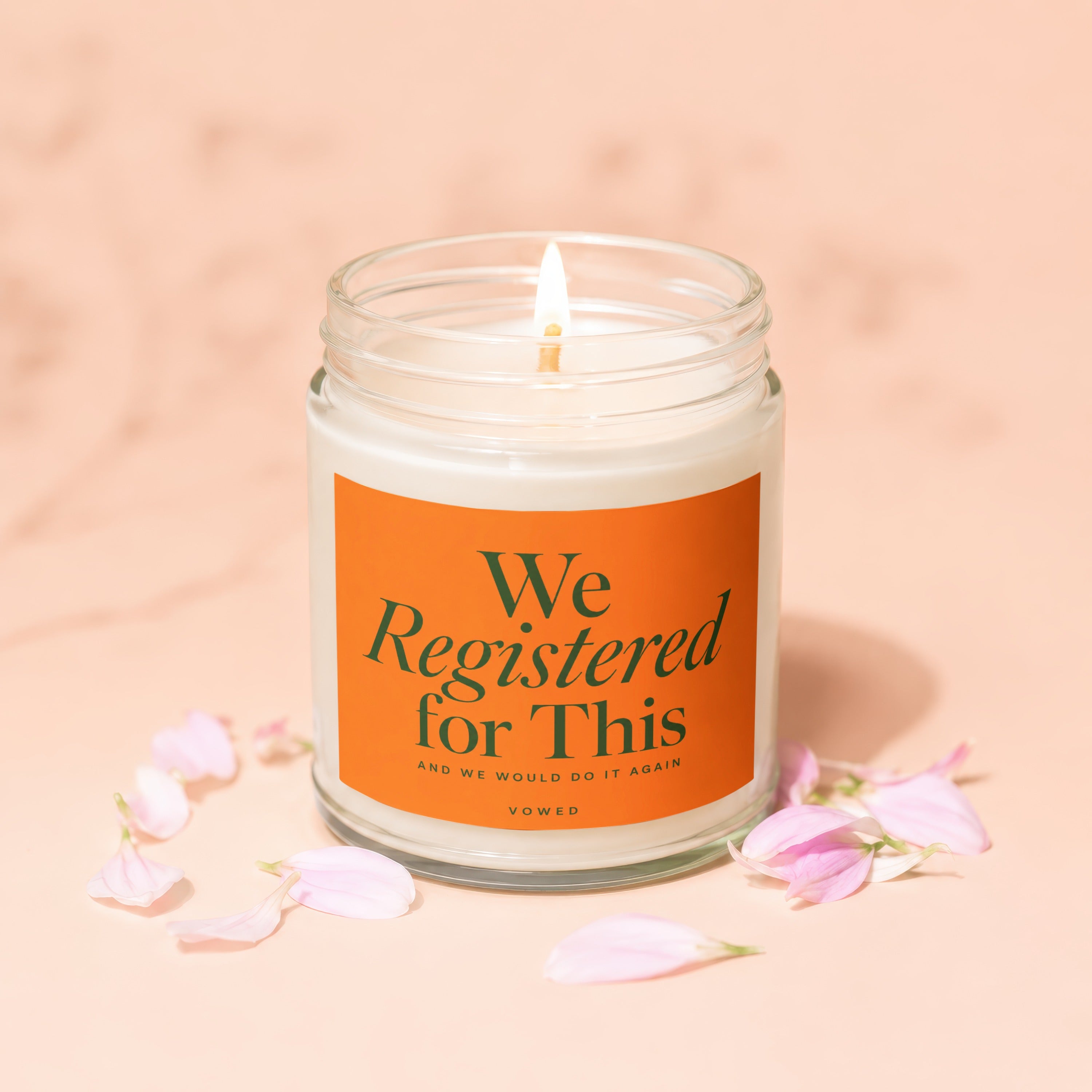 Jar candle with orange label saying "We Registered for This" and a lit wick.