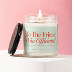 Lit soy candle "To The Friend Who Officiated" on pink background.