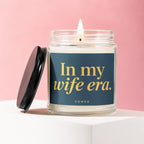 Candle with lid off, lit wick, and text "In my wife era. VOWED."