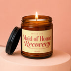 Amber jar candle with lit wick, black lid, and "Maid of Honor Recovery" label.