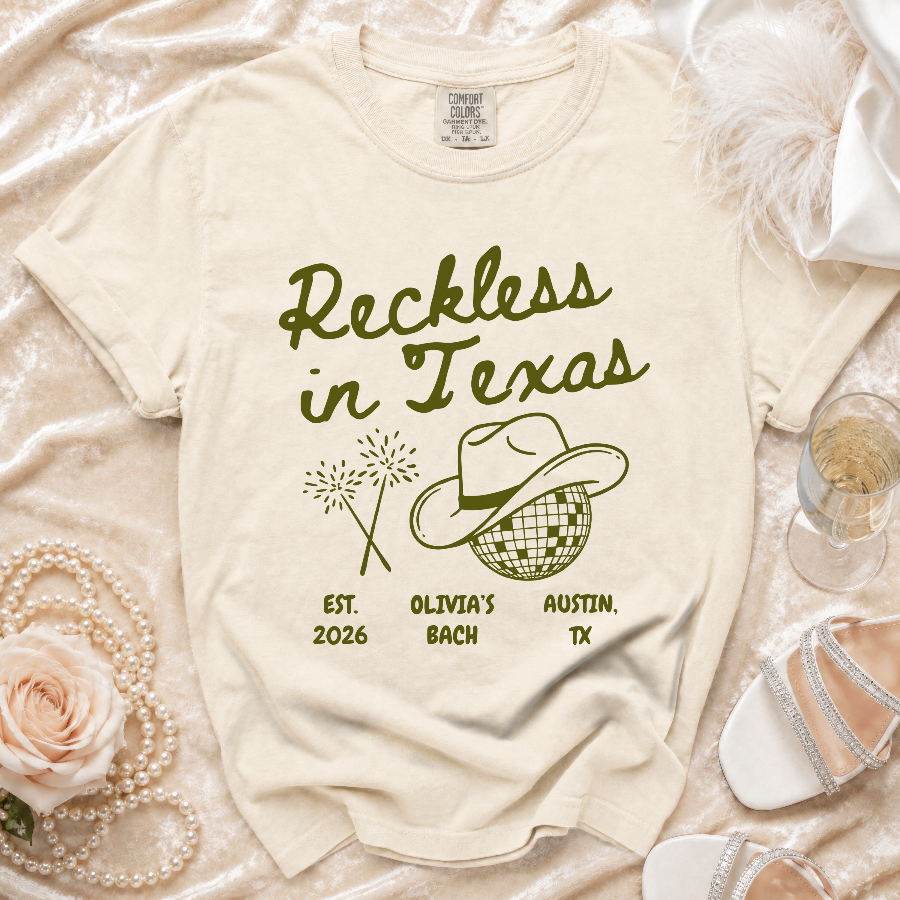 Cream t-shirt with "Reckless in Texas" text, cowboy hat, and fireworks.