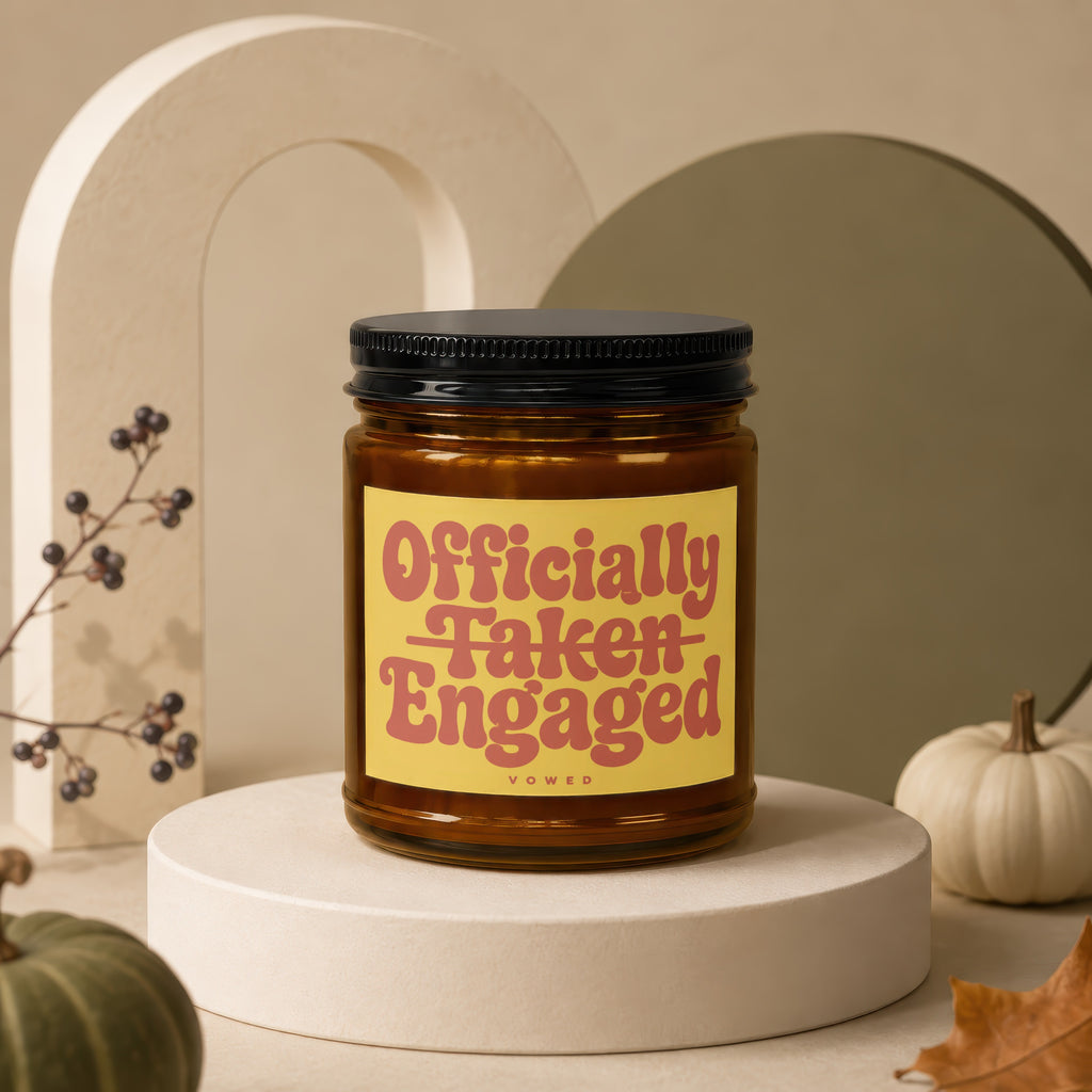 Amber jar candle with black lid, yellow label reading "Officially Taken Engaged"