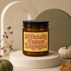 Amber jar candle with black lid, yellow label reading "Officially Taken Engaged"
