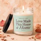 Lit candle in glass jar with lid asks "Smells Like Love Made This House a Home".