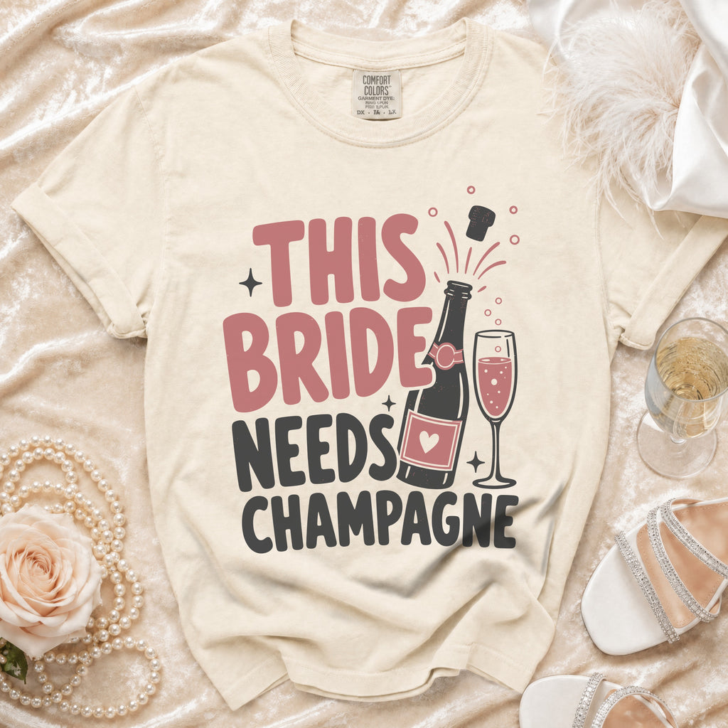 T-shirt with "This Bride Needs Champagne" text, champagne bottle, and glass.