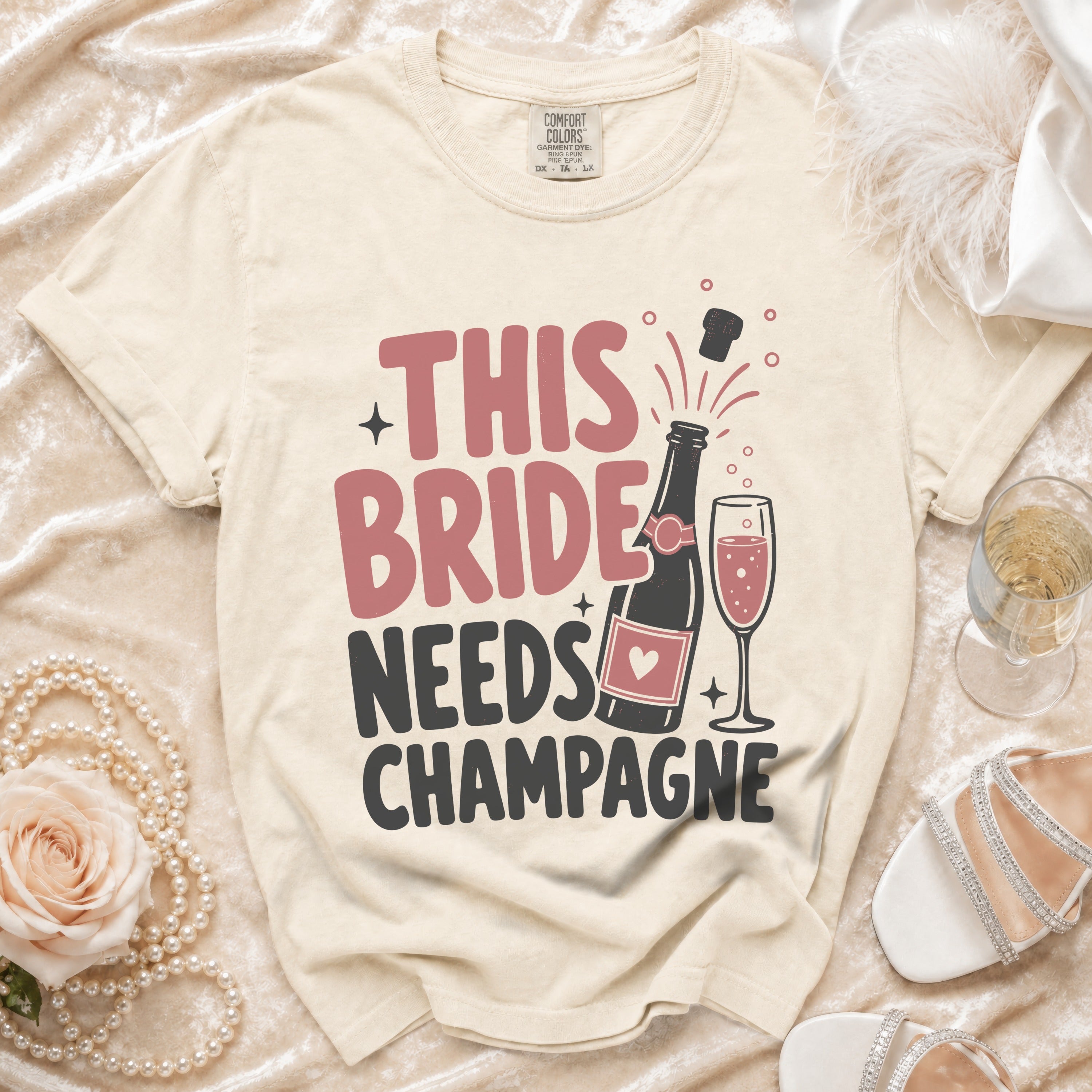 T-shirt with "This Bride Needs Champagne" text, champagne bottle, and glass.