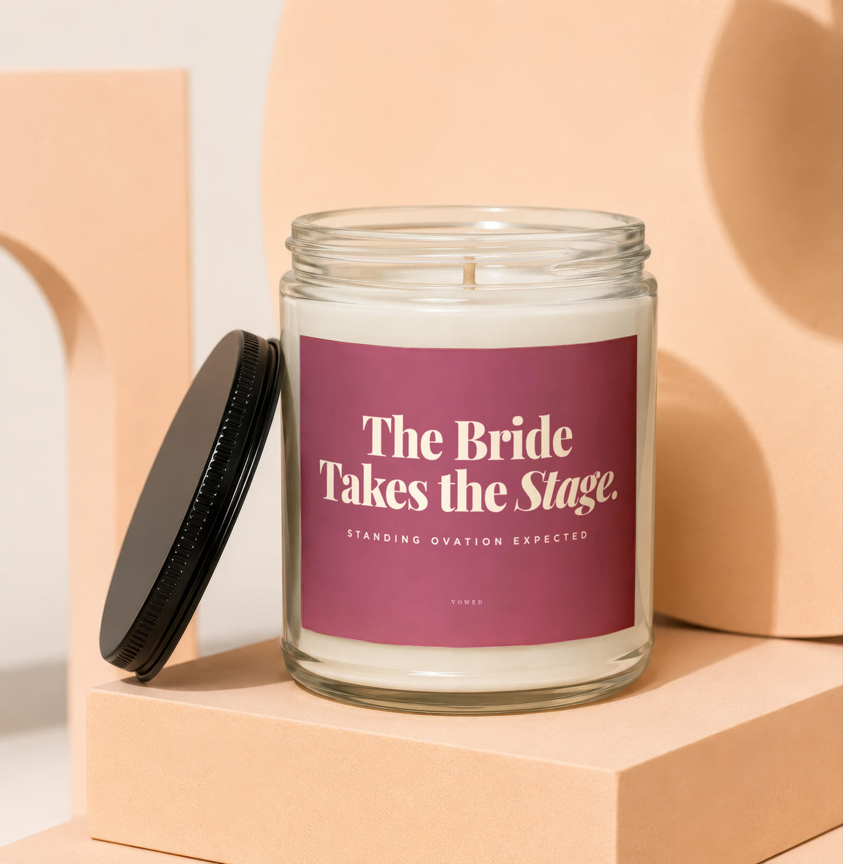 Glass candle with burgundy label reading "The Bride Takes the Stage."
