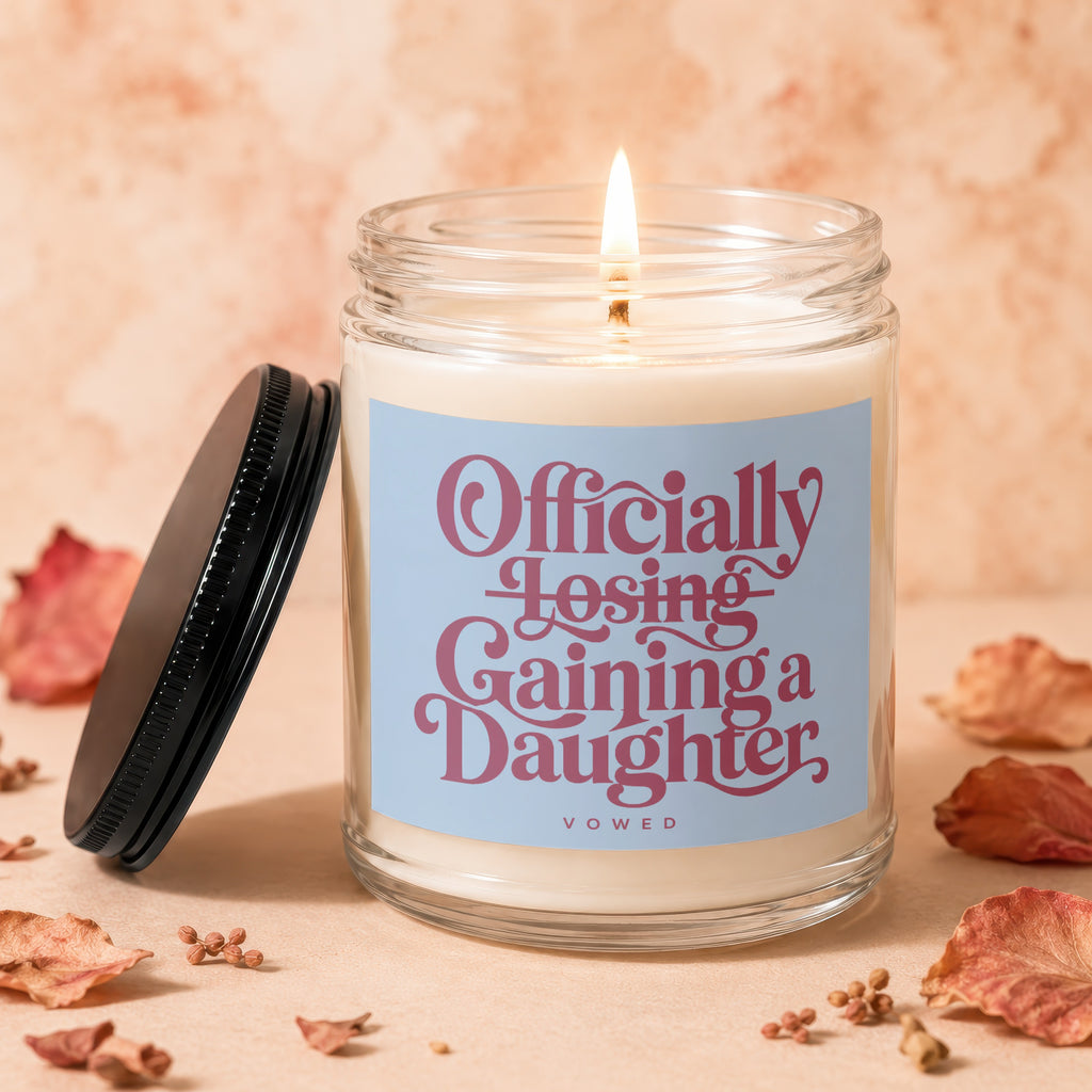 Candle with lit wick and label reading "Officially Losing, Gaining a Daughter."