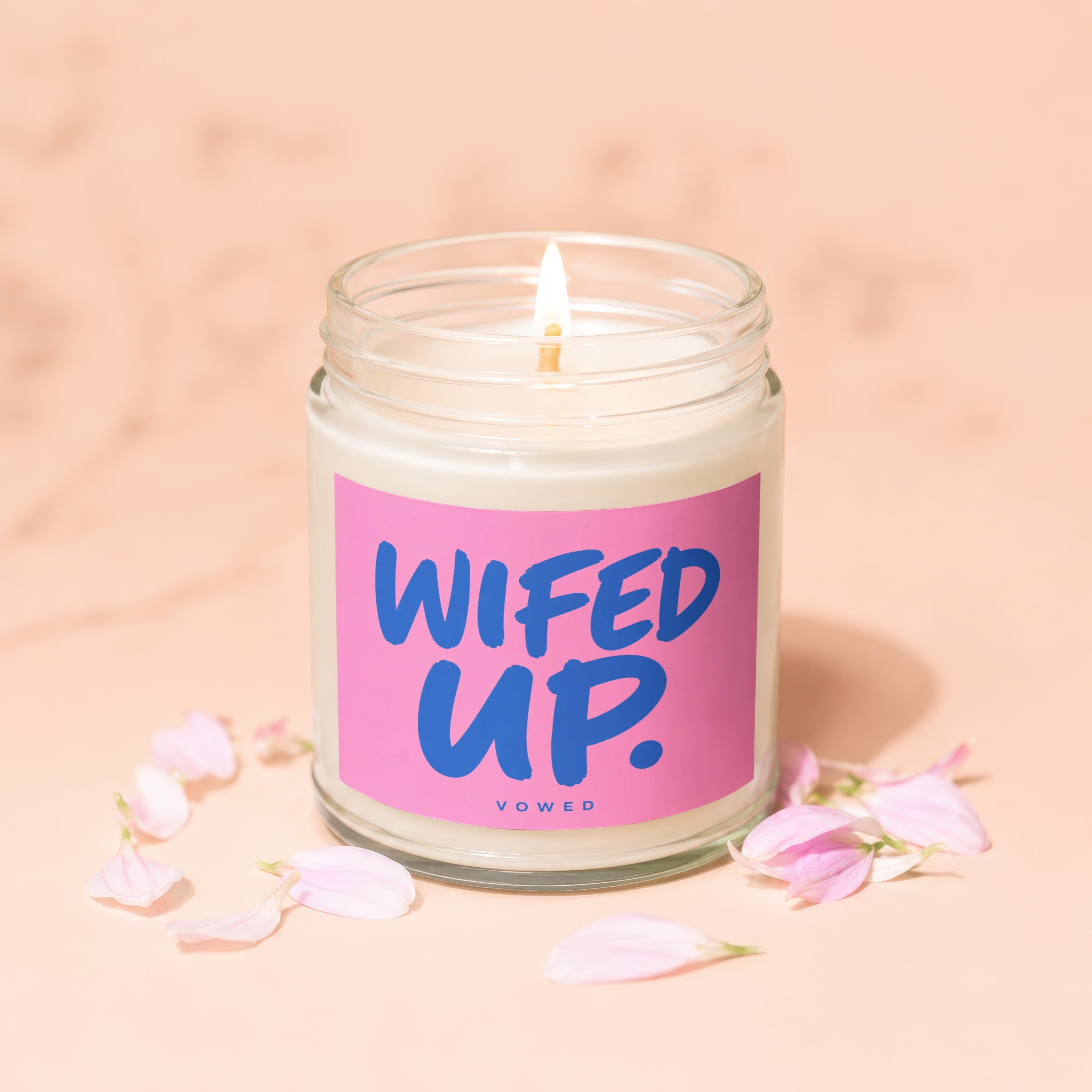 Lit candle in glass jar with pink label reading "WIFED UP. VOWED".