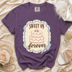 Purple t-shirt with a graphic of a two-tier cake and the words "Sweet On Forever".