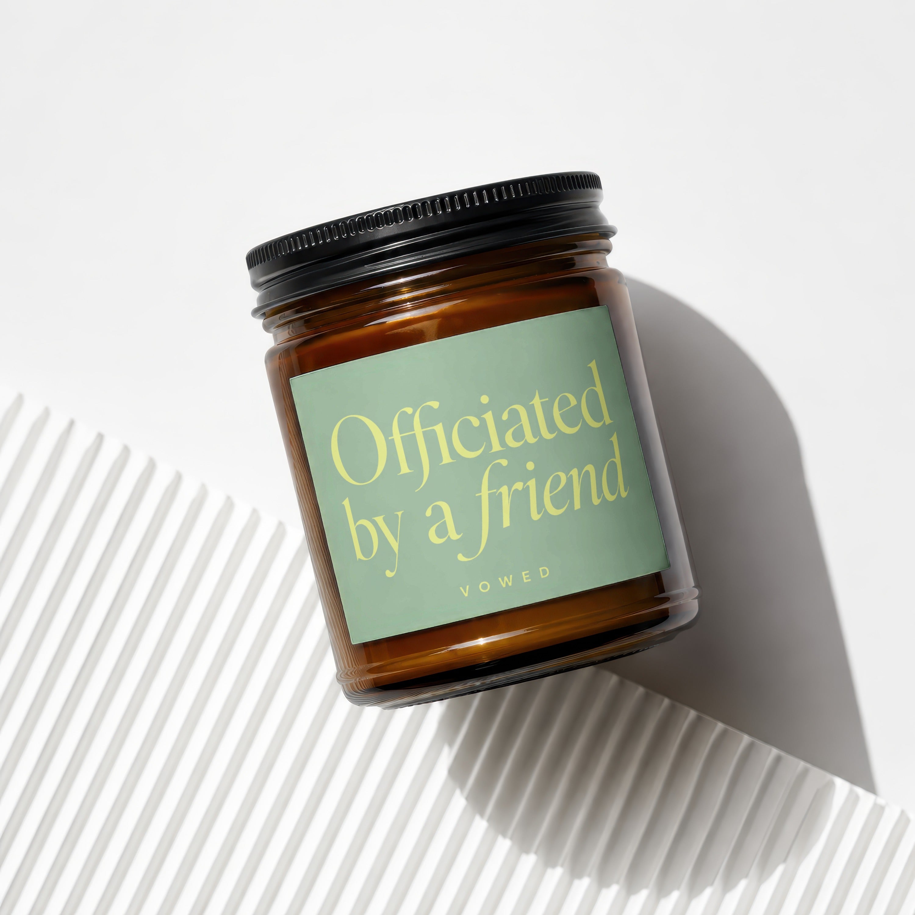 Amber jar candle with "Officiated by a friend" in yellow text on a green label.