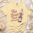 Yellow t-shirt with "This Bride Needs Champagne" text and champagne bottle graphic.