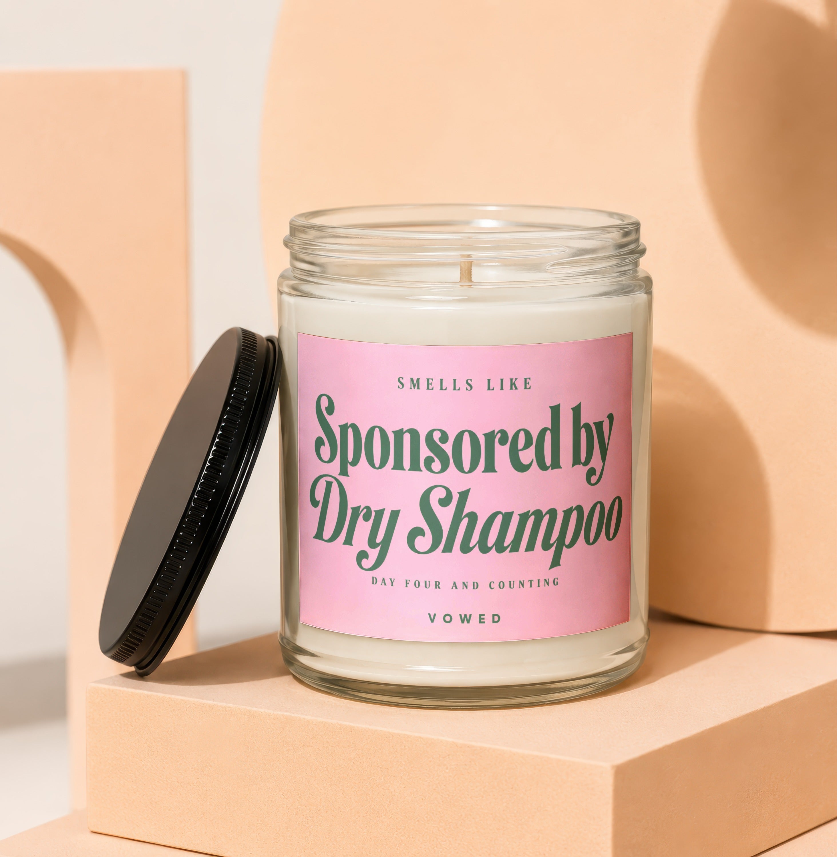 Glass jar candle with pink label that says "Smells Like Sponsored by Dry Shampoo".