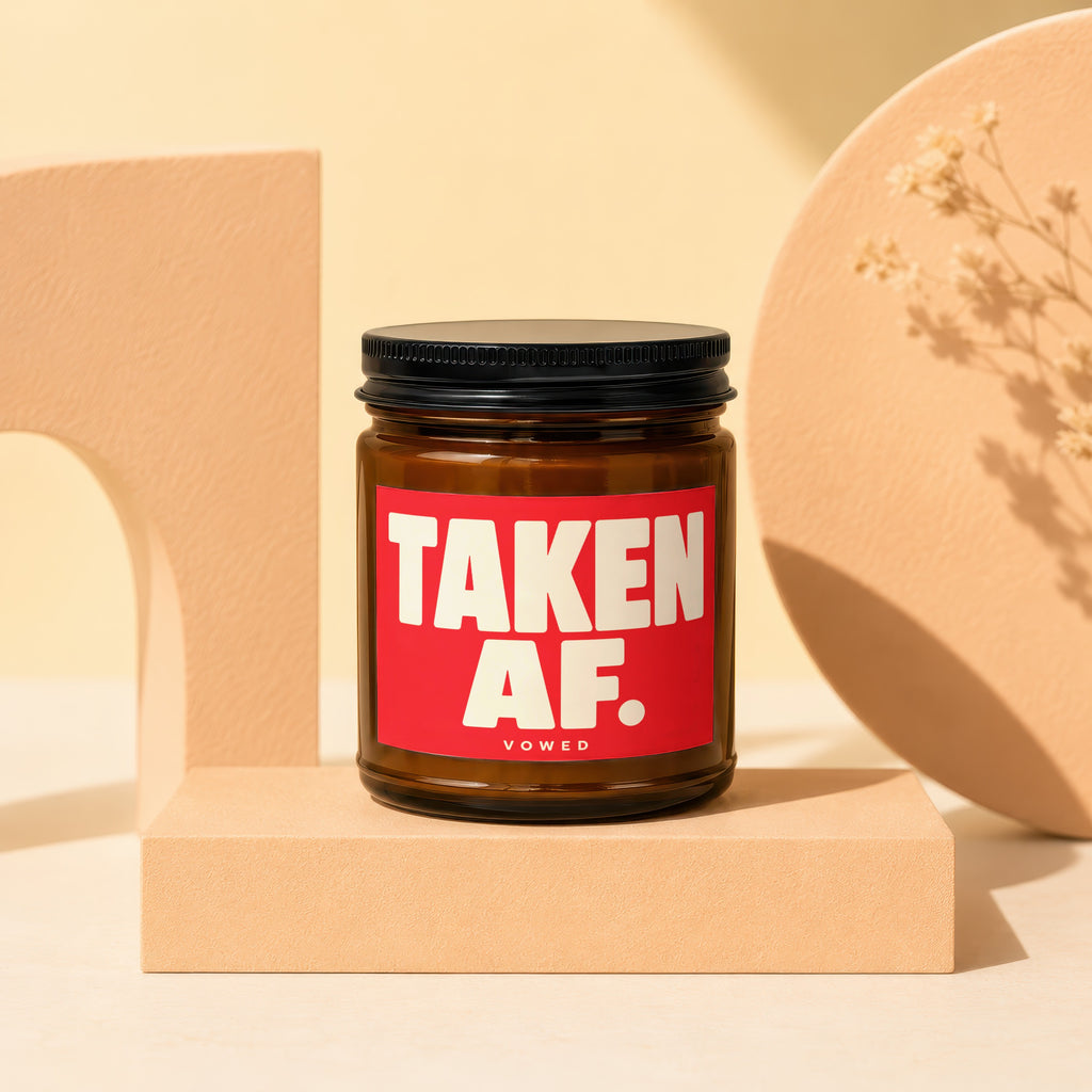 Amber jar candle with red label saying "TAKEN AF. VOWED" on a pedestal.