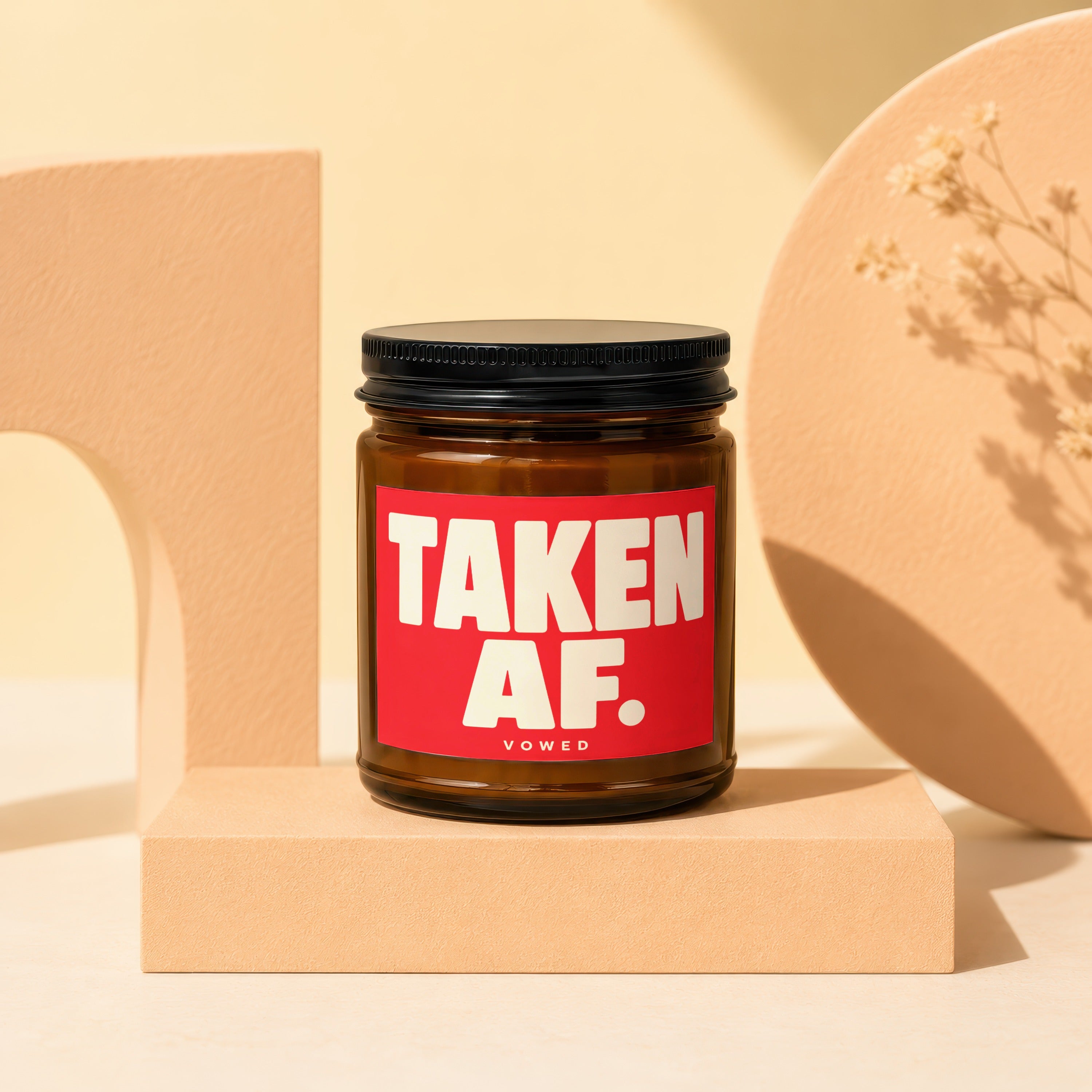 Amber jar candle with red label saying "TAKEN AF. VOWED" on a pedestal.