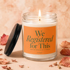 Lit glass candle with orange label reading "We Registered for This" and "Vowed".