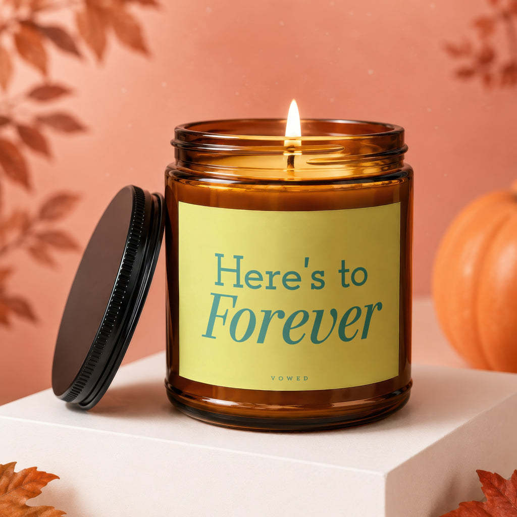 Amber jar candle with lit flame, "Here's to Forever" text, and pumpkin.