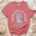 Red t-shirt with "Reckless in Texas" and cowboy boot graphic.