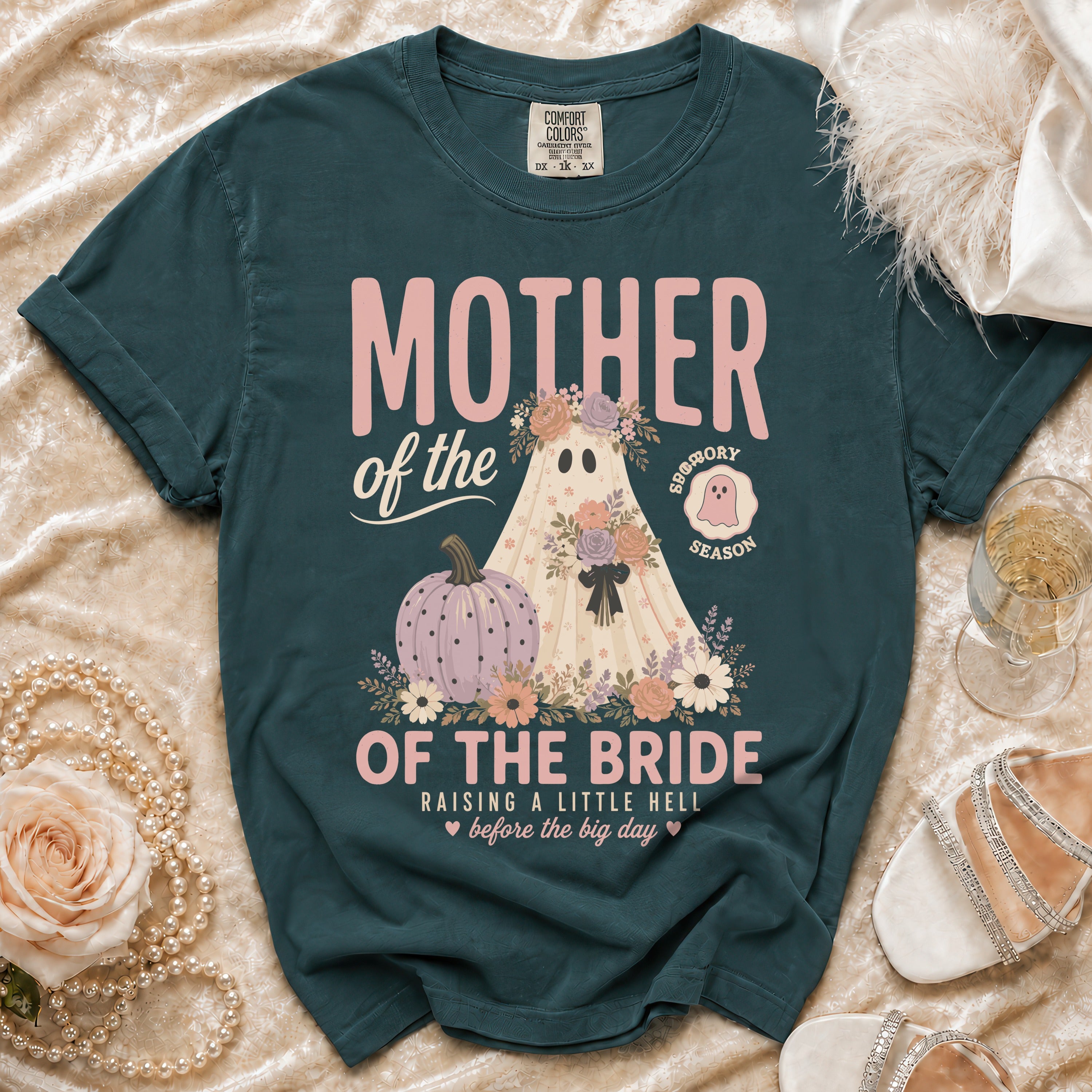 Dark green t-shirt with pink and white text reading "MOTHER OF THE BRIDE," featuring a ghost graphic, pumpkin, and floral elements.