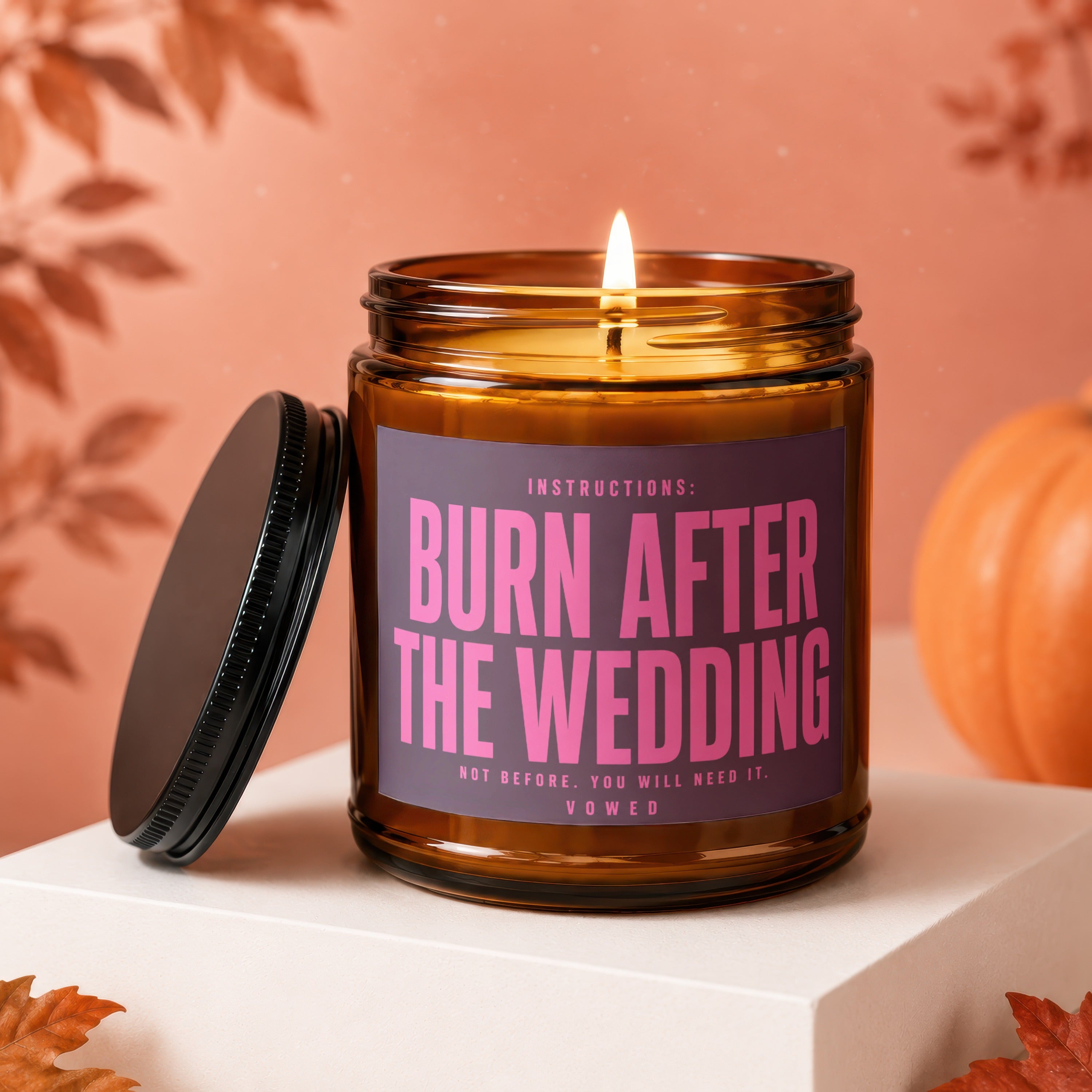 Amber jar candle with lid off, reads "BURN AFTER THE WEDDING" in pink text.