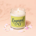 Lit candle in a jar with "Engaged AF" and "VOWED" text, surrounded by petals.