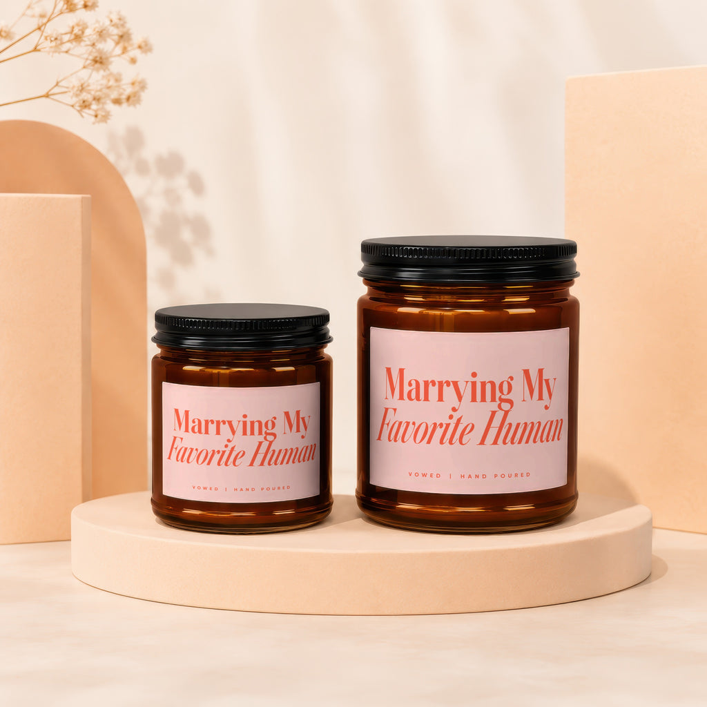 Two amber glass candles with pink labels reading "Marrying My Favorite Human."