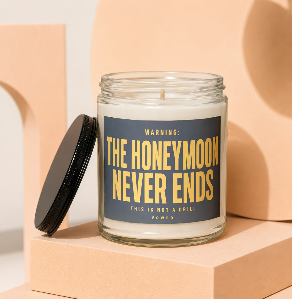 Glass jar candle with black lid, features "WARNING: THE HONEYMOON NEVER ENDS" text.