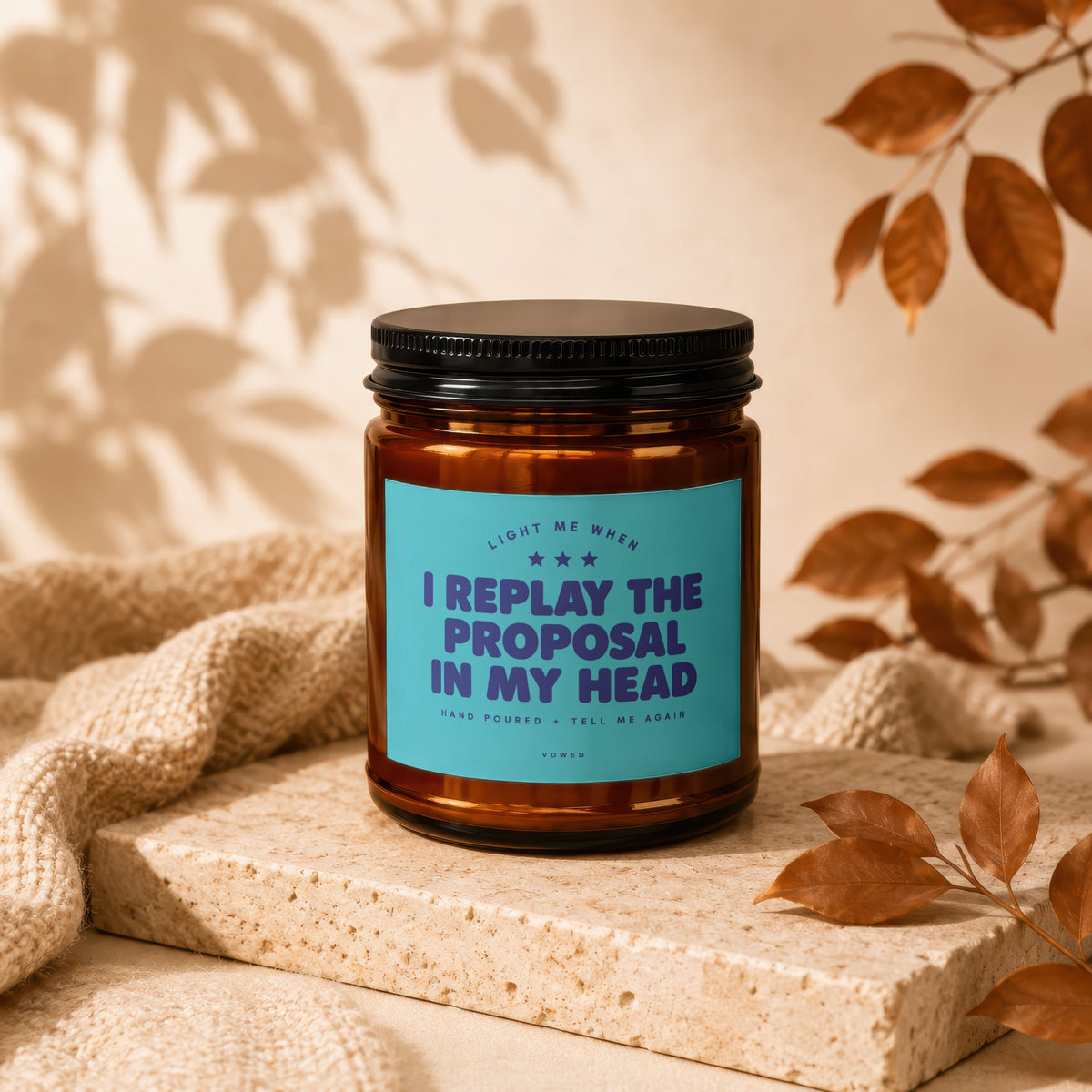 Amber jar candle with blue label reading "I REPLAY THE PROPOSAL IN MY HEAD".