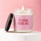 Candle with pink label reading "It's Giving Future Mrs."