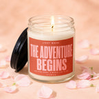 Candle with label "The Adventure Begins" surrounded by pink petals.