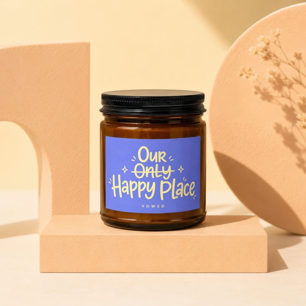 Amber candle with black lid and blue label reading "Our Only Happy Place Vowed".